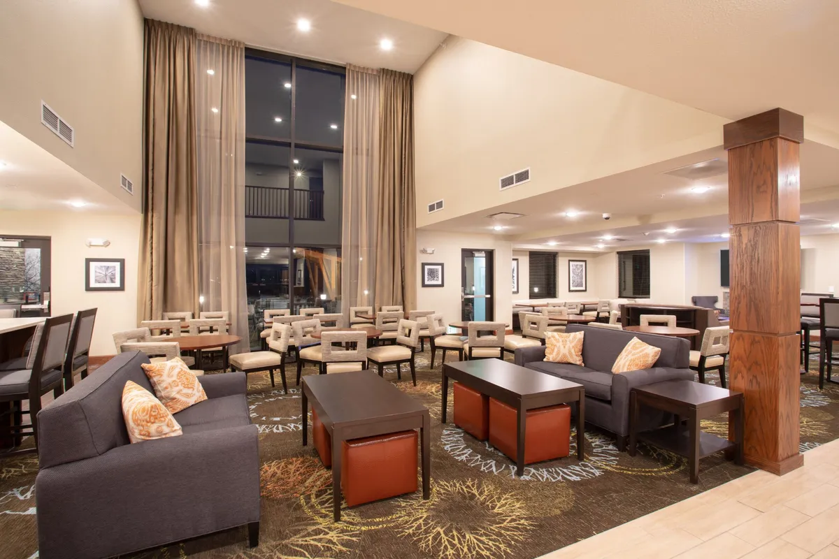 An inviting living area bathed in natural light from large windows. Multiple comfortable seating areas are arranged around decorative pillows, creating a welcoming space perfect for relaxing, reading, or socializing. The decor is modern and warm, emphasizing comfort and versatility.