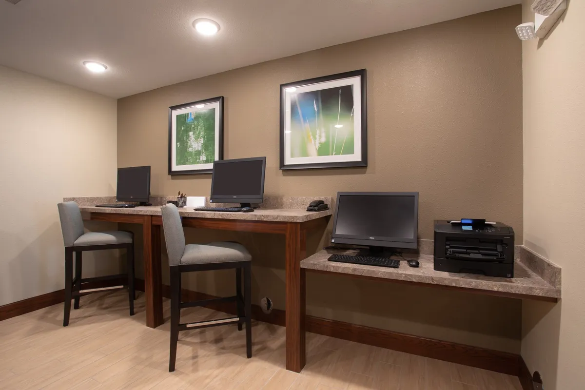 A bright, well-organized business center featuring computer workstations, a printer, and modern artwork. The space is designed for productivity, with ample desk space and comfortable chairs, ideal for business travelers or remote workers.