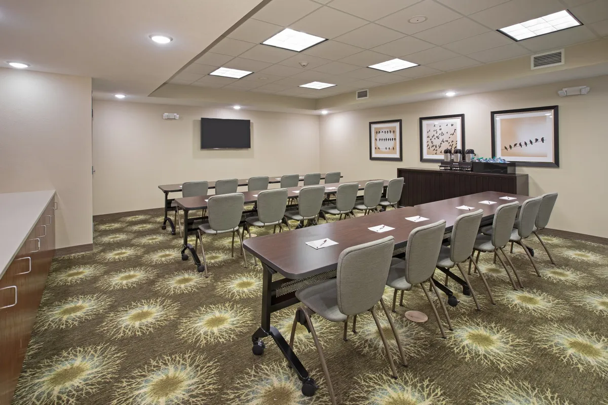 This image showcases a spacious interior with long tables arranged in a U-shape, comfortable chairs, decorative wall art, and a television screen. The setup encourages group activities and gatherings, emphasizing versatility for different types of events or family meals.