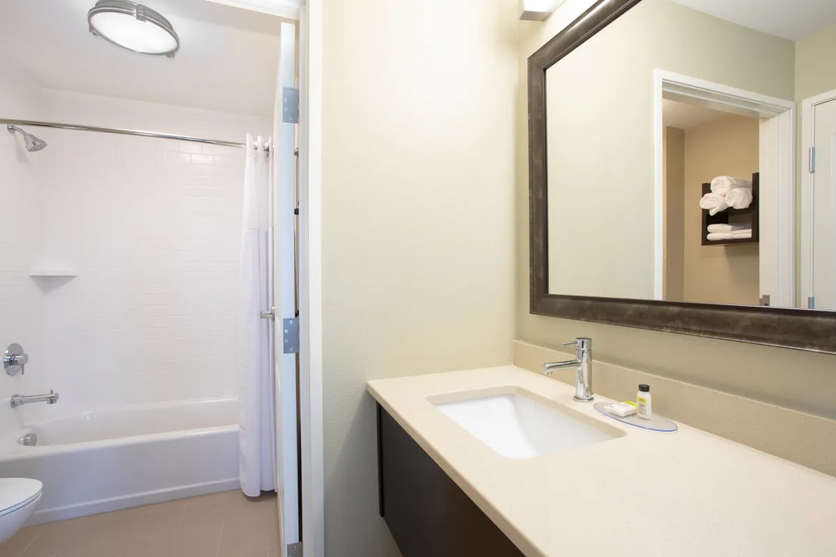 A modern bathroom scene featuring a well-lit sink with a mirror and a spacious bathtub. The space is tidy and uncluttered, with fresh towels artfully placed, evoking a sense of cleanliness and comfort. The atmosphere is bright and refreshing, ideal for unwinding after a busy day.