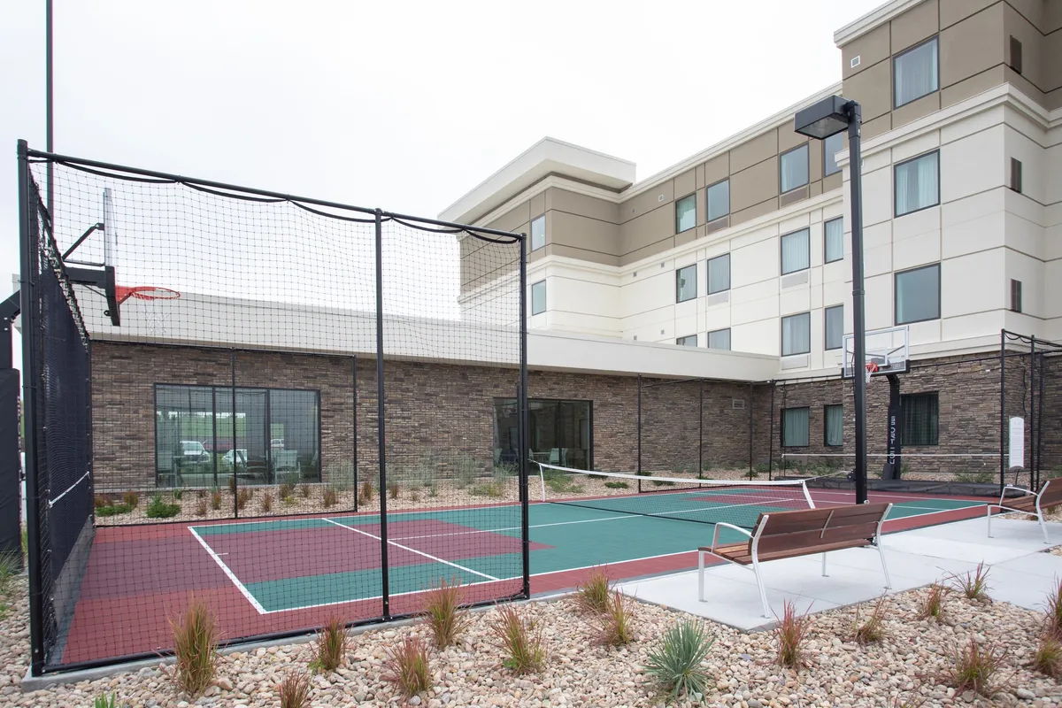 This exterior image captures the energetic atmosphere outside the building, featuring an inviting basketball court, the attractive building facade, and landscaped grounds. Guests are seen engaging in friendly matches and casual meet-ups, emphasizing communal activity and accessible amenities.
