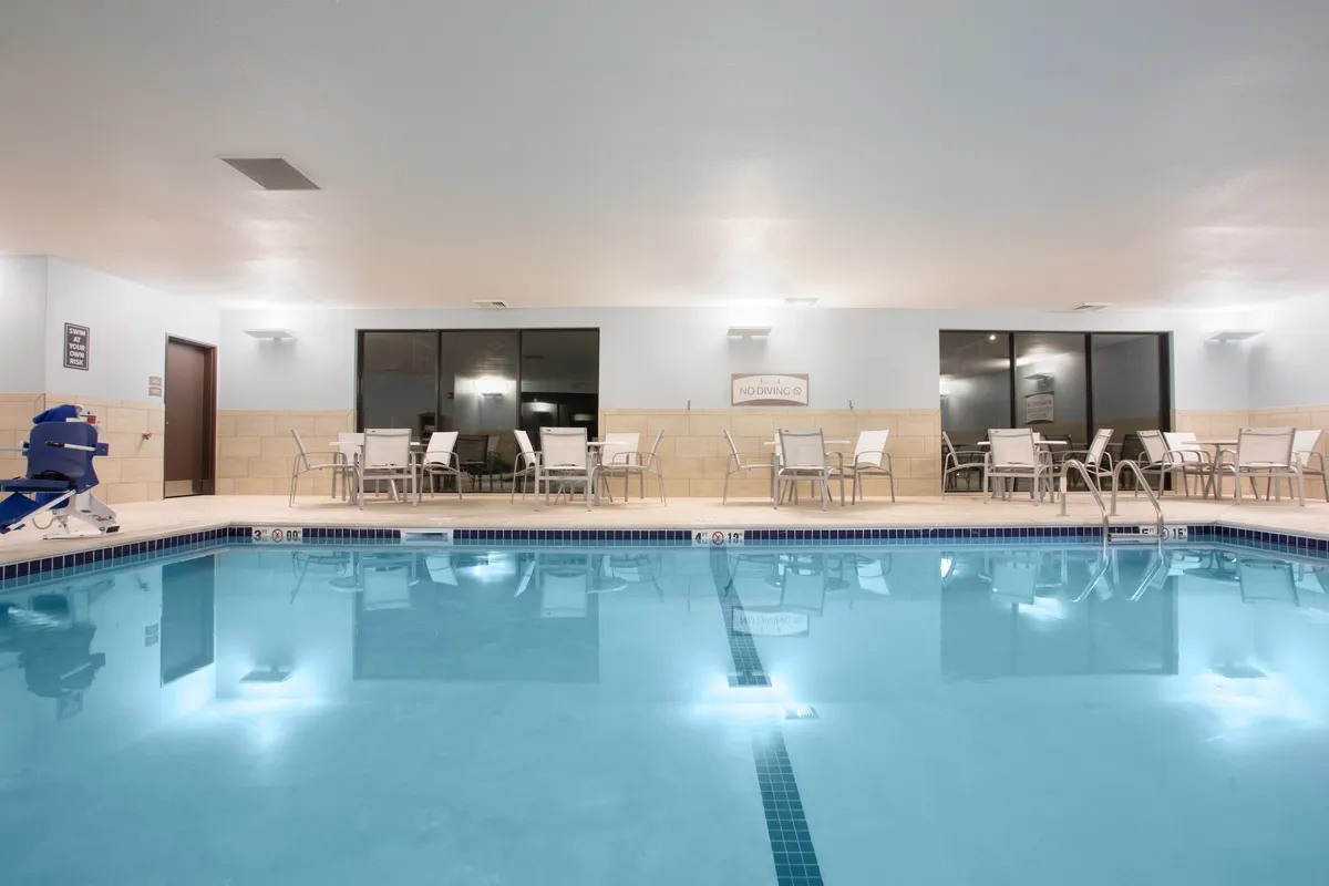 A tranquil indoor swimming pool area features comfortable seating and large windows, offering a peaceful spot for relaxation or socializing. The bright, clean environment highlights shared amenities enjoyed by all guests.