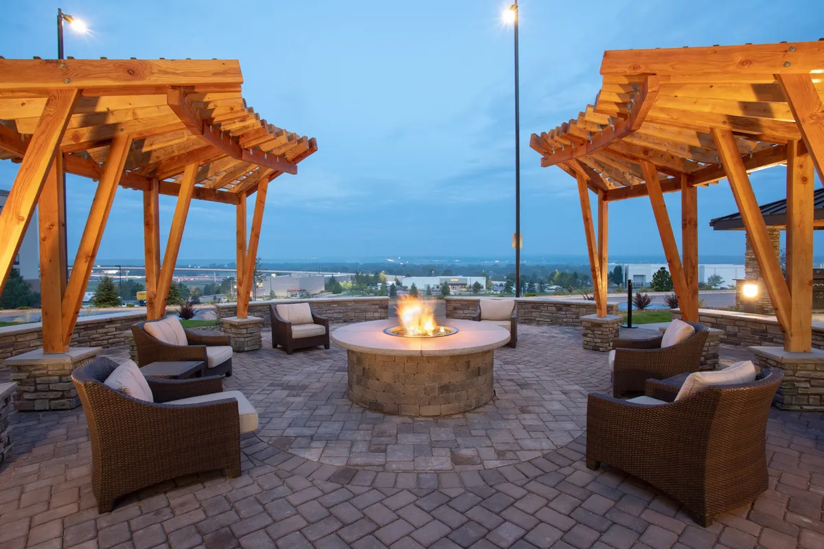 A relaxed outdoor gathering area with a fire pit, wooden pergolas, and comfortable seating. Guests enjoy evening conversations, stargazing, and unwinding after a productive day, suggesting a seamless transition from business to relaxation in the same location.