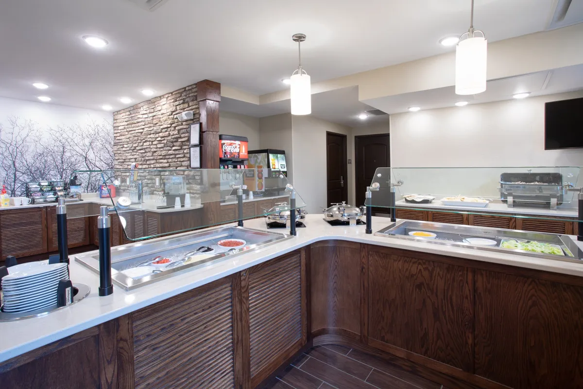 A bright and inviting buffet counter stands against a textured stone wall, with an abundant food display under warm lighting. The area is arranged for guests to easily serve themselves and gather for a relaxed meal, with a sense of communal dining and social interaction.